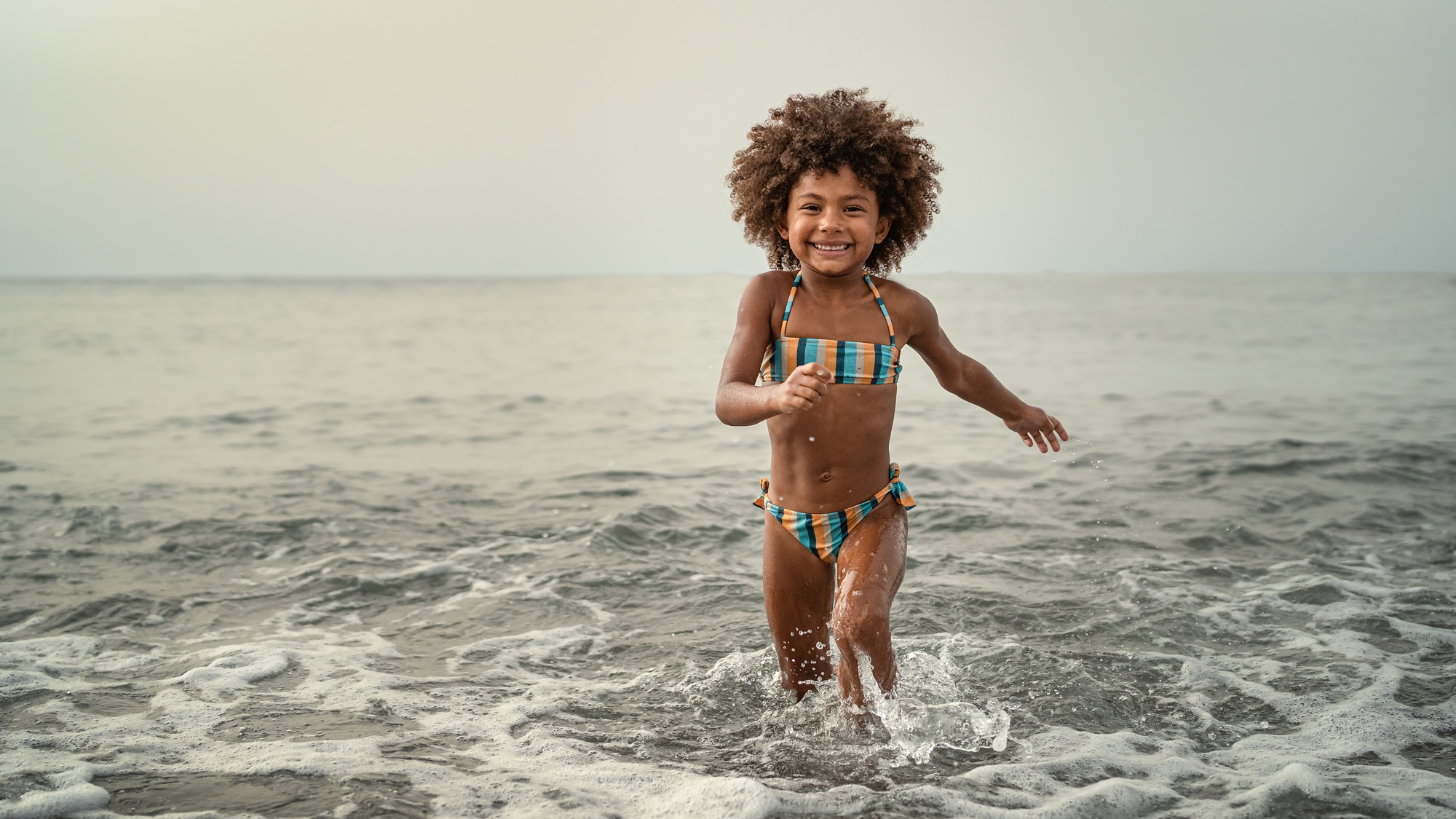 Afro child having fun playing inside sea water during summer holidays