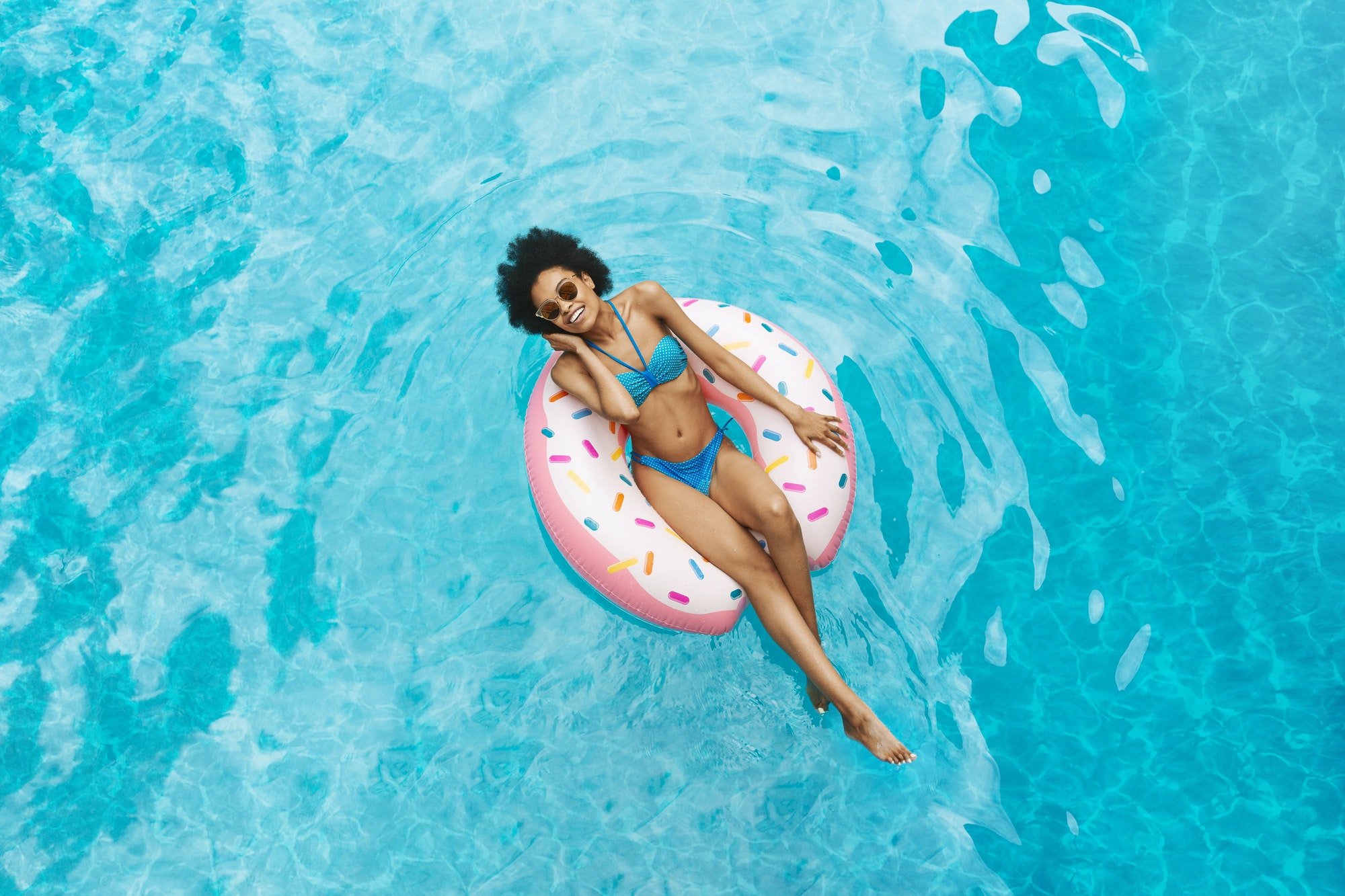 Millennial African American girl in sexy swimwear floating on donut ring at pool